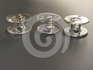 Three transparent plastic sewing machine bobbins. Textile industry. Detail of sewing equipment. Gray background, back lighting