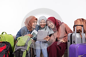 Three traveler veiled women holding tablets while jokingly sitting on the couch