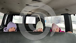 Three triplet sisters ride in winter on the back seat of a big car on their hats