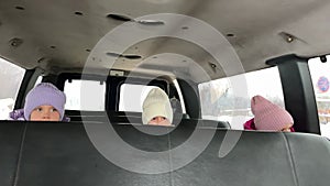 Three triplet sisters ride in winter on the back seat of a big car on their hats