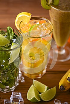 Three tropical mixed drinks, mint, lemon and kiwi fruit cocktails served on light wooden table.