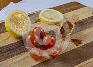 three and two half of cherry tomatoes with half lemon lemon slice and scoop with red pepper spice on wooden cutting board
