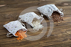 Three types of cereals buckwheat, rice and lentils in canvas bags. They lie on a wooden background.