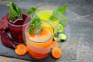 Three types of organic vegetable juice with ingredients on slate