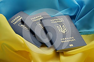 Three Ukrainian biometrical passports on folded waving flag of Ukraine country