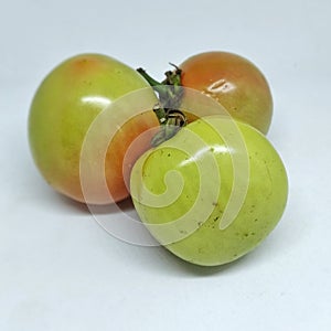 three unripe but fresh looking tomatoes on a white background