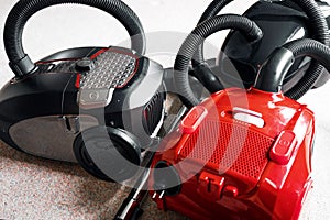 Three vacuum cleaners in different colors sitting on a white carpet floor.