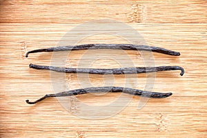 Three vanilla pods aligned on wood