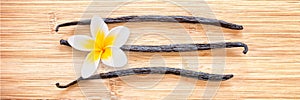 Three vanilla pods with a flower aligned on wood panoramic background
