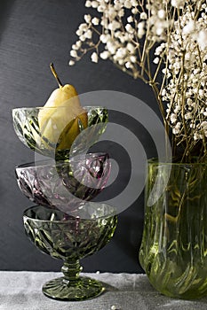 Three vases for cream of dark green and purple glass stand on top of each other. In the last there is a big pear