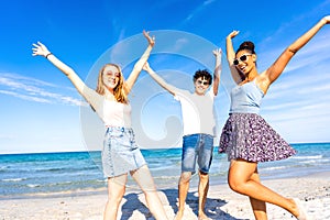 Three very happy friends having fun at the beach posing laughing looking at camera for a portrait with raised arms. Gen z photo