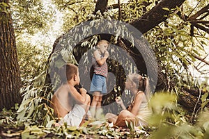 Three village children are playing in a hut which they themselves have built from leaves and twigs. Wooden house in the forest