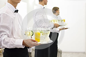 Three waiters in bow ties holding trays.