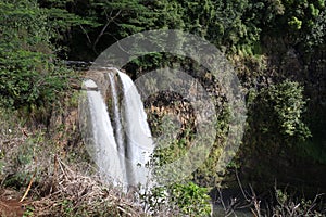 Three waterfalls cascading over a volcanic cliffside surrounded by rain forest at Wailua Falls in Kauai, Hawaii