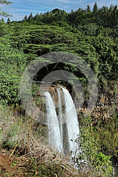 Three waterfalls cascading over a volcanic cliffside surrounded by rain forest at Wailua Falls in Kauai, Hawaii