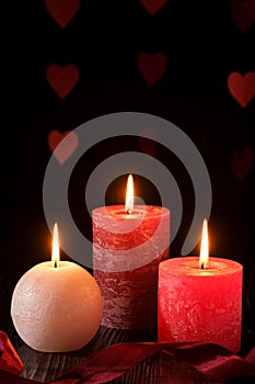 Three wax flame candlelight with ribbon in dark romantic light on hearts background