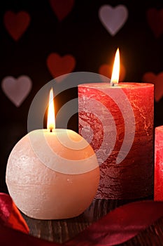 Three wax flame candlelight with ribbon in dark romantic light on hearts background