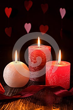 Three wax flame candlelight with ribbon in dark romantic light on hearts background, love dating, Valentine`s day