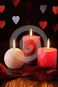 Three wax flame candlelight with ribbon in dark romantic light on hearts background, love dating, Valentine`s day