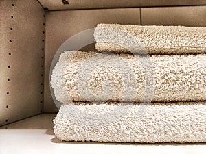 Three white bath towels are neatly folded and stacked in a cabinet