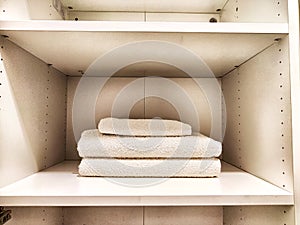 Three white bath towels are neatly folded and stacked in a cabinet