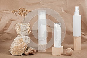 Three white blank cosmetic tube with cream, lotion or shampoo, stones, geometric shape, dried plant flowers on beige craft paper