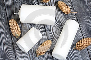 Three white candles lie on painted pine boards. Spruce cones are spread out nearby