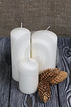Three white candles stand on painted pine planks. Spruce cones are spread out nearby