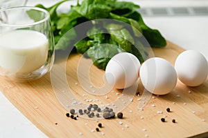Three white chicken eggs on a cutting board with a bunch of fresh spinach
