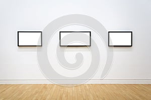 Three white clipped paintings with wooden frames hung on a clear wall.