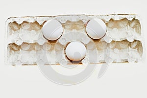 Three white eggs in a cardboard tray on a white background