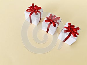 Three White gift boxes red ribbon bow on beige background, copy space.