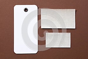 Three white and gray cardboard rectangular blank tags for clothes positioned in center of brown background with white