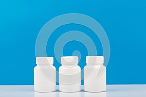 Three white medication bottles against blue background. Concept of vitamins, supplements, medication and healthcare