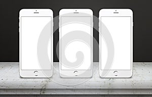 Three white mobile phones on table with blank, white, isolated display screen for mockup