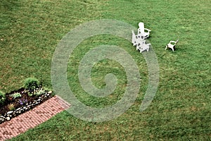 Three white and one tan lawn chairs on a large lawn.