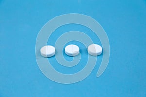 Three white round pills on blue background. Concept of healthcare and medicine communication