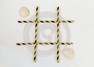 Three white seashells are lined up in a tic-tac-toe pattern on a white background. The grid consists of colored tubes from a