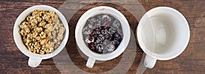 Three white single serving bowls with blackberry crumble dessert, on a wood background