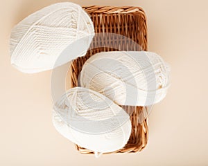 Three white skeins of yarn and a wicker basket. Nice photo for a hobby, vertical orientation. Hobby aesthetics.