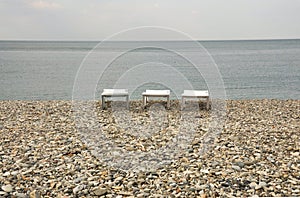 Three white trestle beds stand on the stone seashore