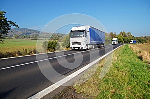 Three white trucks on the road in the countryside