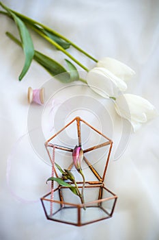 Three white tulips, a tulip bud in a decorative design made of metal, a coil with a pink ribbon