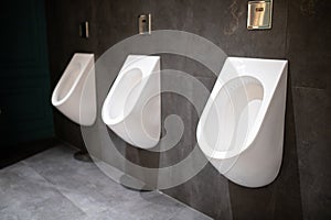 Three white urinals hanging on the wall in a dark luxury public toilet