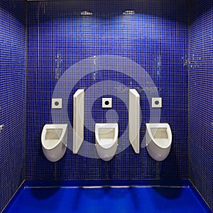 Three white urinals in men public toilet against blue wall.