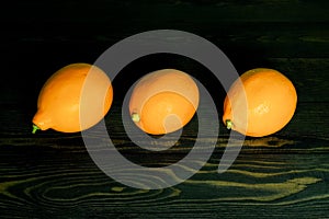 Three whole bright yellow lemons laid out on a rough wooden authentic background