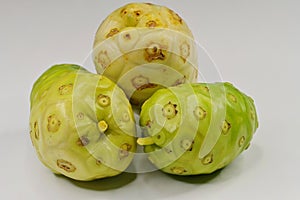 Three whole Noni fruits, Morinda citrifolia, against white background