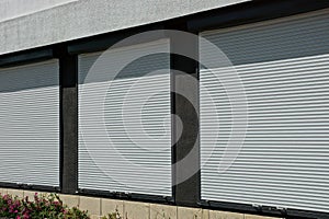 Three windows covered with white plastic shutters on the wall of the house