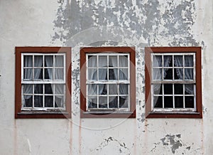 Three windows on the shabby wall closed with curtains