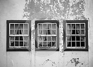 Three windows on the shabby wall closed with curtains